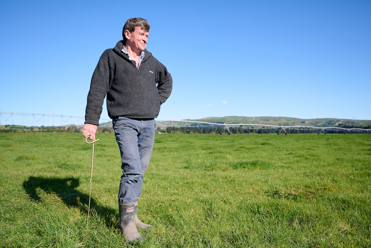 Robb Macbeth standing in a green paddock leaning on a gold coloured standard, with a irrigator behind him