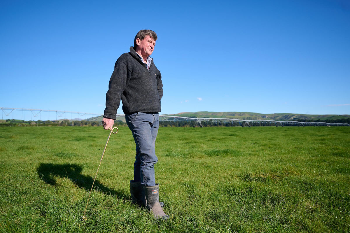Robb Macbeth standing in a green paddock, leaning on a gold-coloured standard, with an irrigator behind him.
